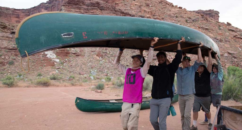 A group of students carry a canoe over their heads. 